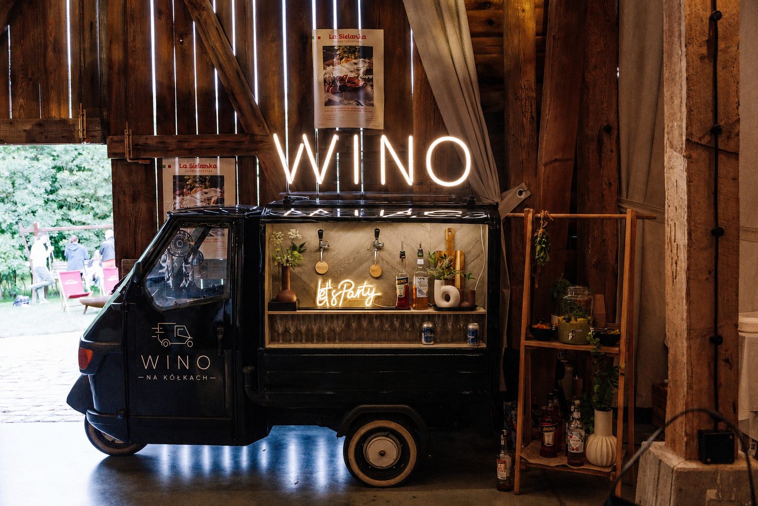 Czarny van Wino na kółkach we wnętrzu rustykalnej stodoły eventowej